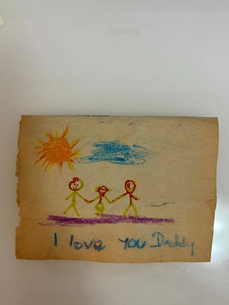 Original crayon drawing on worn paper with a family under the sun and the words I love you Daddy.